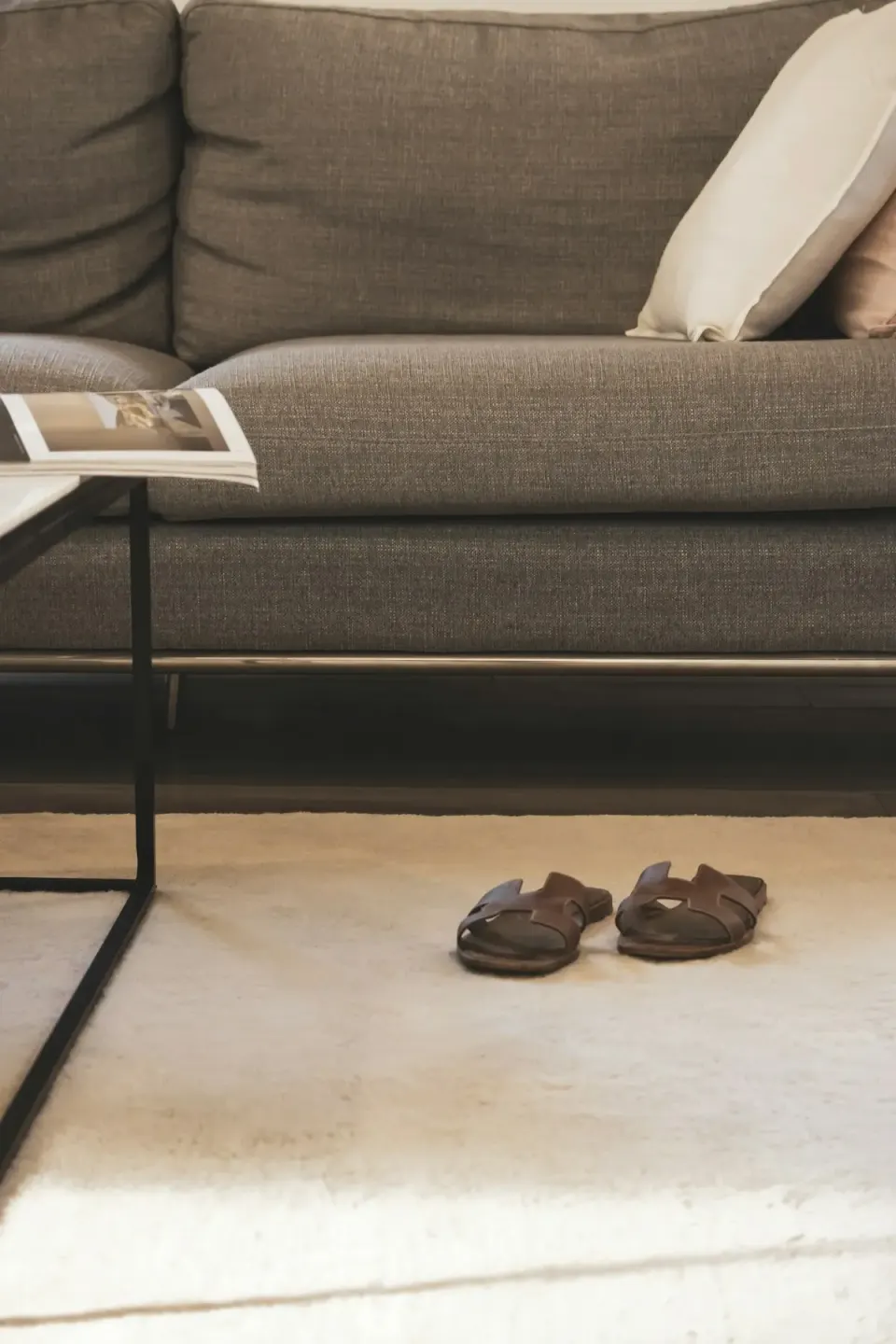 Une paire de chaussons au pied d’un canapé, dans un salon calme.
